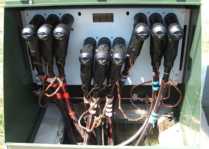 Grey switch with cables attached to the front in a green cabinet